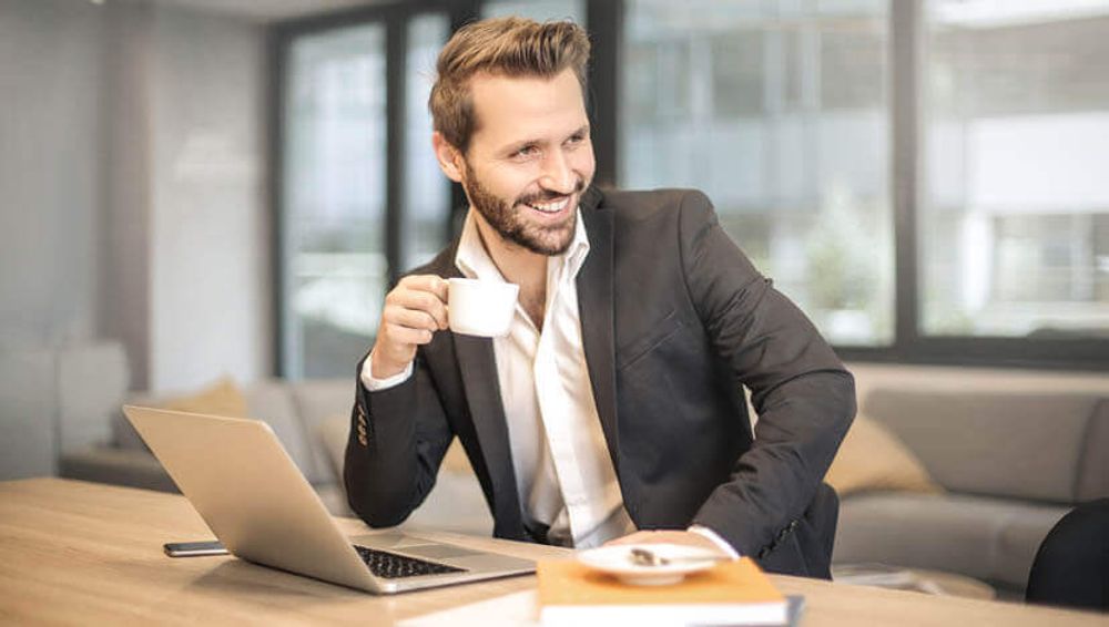 a man sitting at a table with a laptop and a cup of coffee